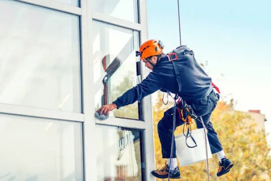 Rope-access technician washing commercial building glass