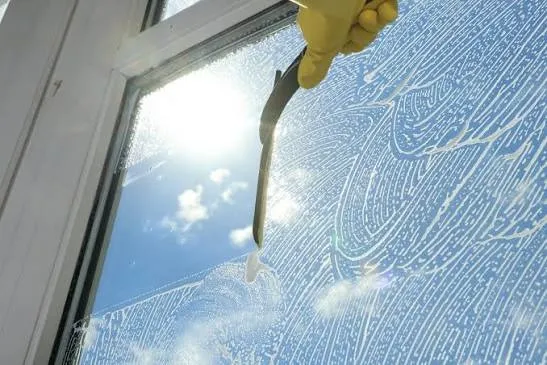 Gloved hand squeegeeing a soapy window on a sunny Temecula day
