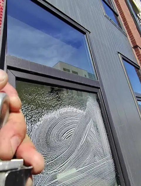 Close-up of a technician scrubbing an exterior window with a dark frame