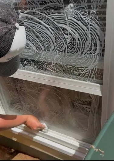 Technician scrubbing a window, leaving soap swirls before the squeegee pass