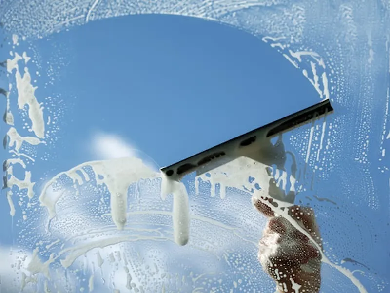 Squeegee clearing a band of foam from window glass against a blue sky