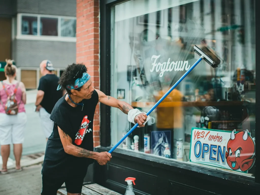 Window cleaner washing a storefront window with a pole and squeegee