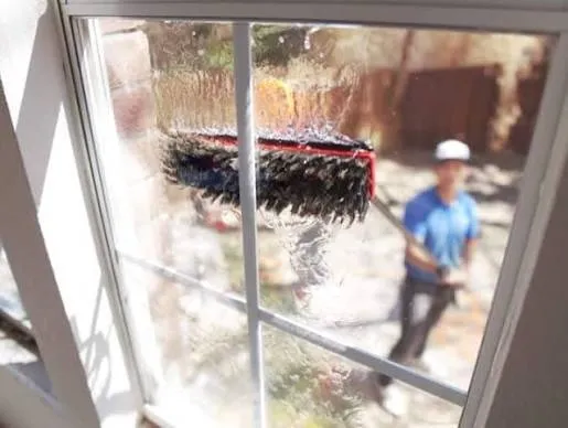 Water-fed pole brush washing an upper window from the ground outside a home