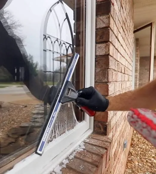 Window cleaner squeegeeing a window on a brick home exterior